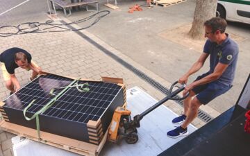 Zwei Menschen laden eine Palette mit Photovoltaik-Anlagen für den Balkon ab